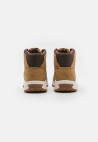 Stivali alla caviglia in suede marrone con un pannello testurizzato marrone scuro, suola bianca e collo imbottito. Presentano un logo discreto sul tallone.