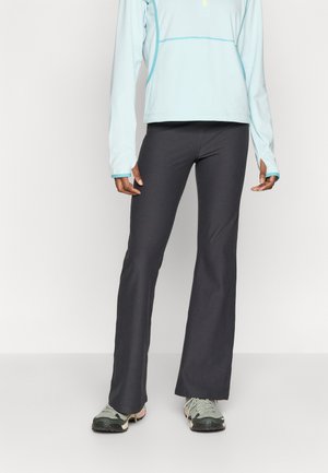 Helehall sinine pikkade varrukatega pluus poollukuga kaelusega, ühendatud tumeda halli lõhenevate sportlike pükstega ja roheliste matkajalatsitega.