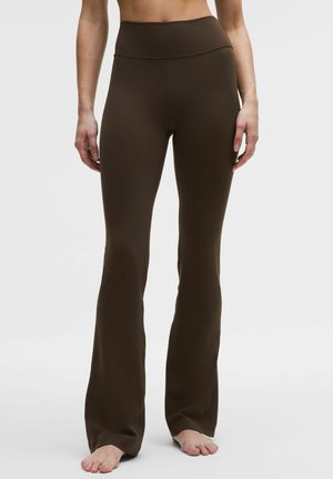 Brązowe legginsy z rozszerzanymi nogawkami wykonane z elastycznego materiału, z wysokim stanem oraz gładką, matową fakturą bez widocznych wzorów czy akcentów.
