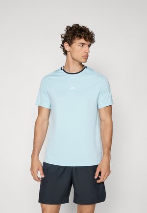 Lyseblå kortermet sports skjorte med rund hals og marineblå detaljer. Har en logo på brystet og en myk, glatt tekstur.