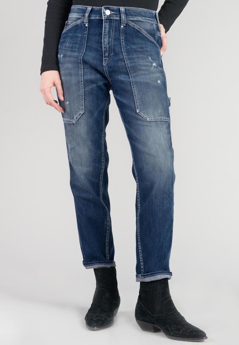 Jeans in denim blu con una vestibilità rilassata, caratterizzati da grandi tasche anteriori, una texture sbiadita e orli arrotolati. Indossati con stivali da cowboy neri.