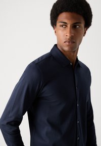 Navy langermet skjorte med krage med knapper, glatt tekstur, stoffet faller elegant, med subtile knapper foran.