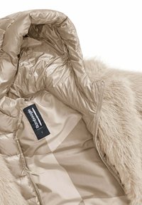 Beige pufferjack met een faux fur voering, glanzend satijnen binnenmateriaal, ritssluiting en een label met de merknaam "Bomboogie".