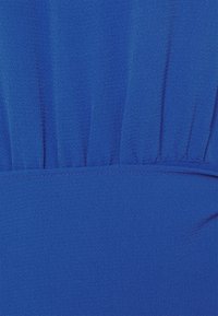 Texturerat stretchtyg i livligt blått, med rynkade detaljer och en slät midja. Fokus på rena linjer och djup färg.