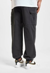 Cargo broek in donkergrijze katoenmix, met elastische boorden, zijzakken en een relaxte pasvorm, gecombineerd met witte sneakers met zwarte accenten.