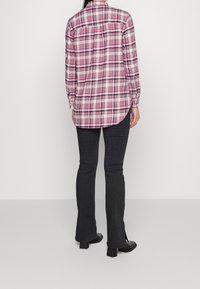 Långärmad rutig skjorta i rosa, vit och svart. Har en rundad nederkant och knäppte manchett. Matchad med mörka utsvängda jeans och svarta klackar.