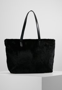 Černá kabelka z umělé kožešiny s hladkými koženými uchy, obdélníkový tvar a měkká textura. Jednoduchý design, žádné viditelné kovové prvky nebo vzory.