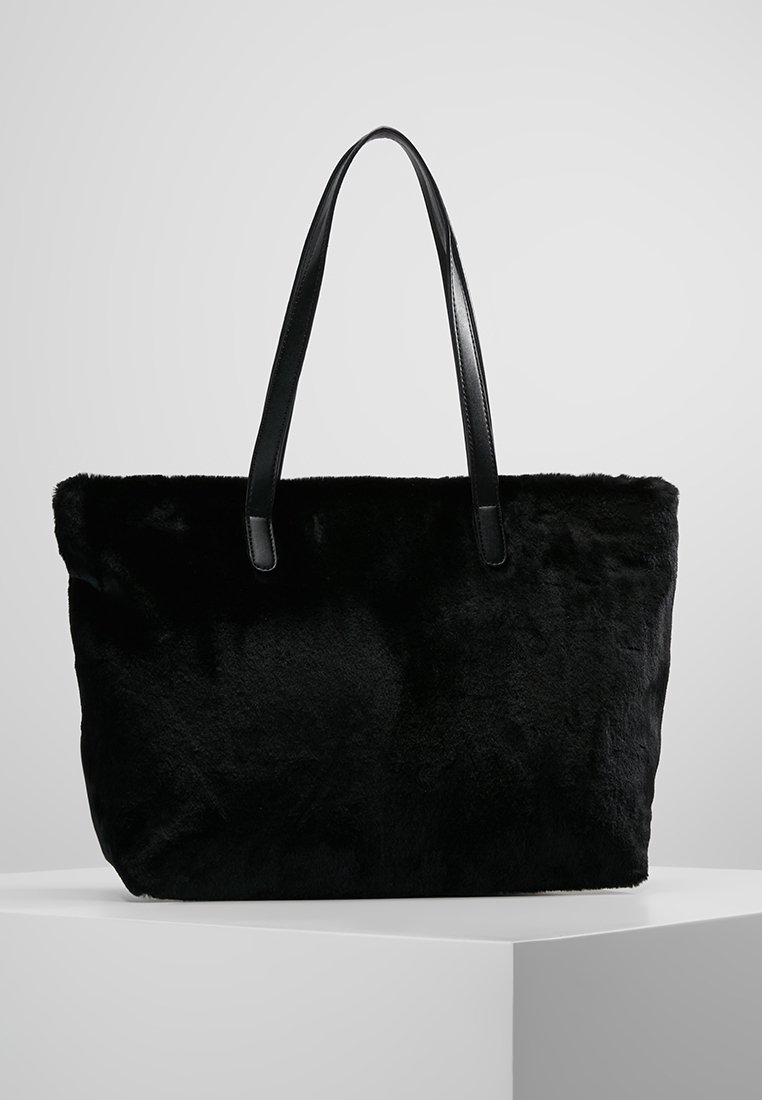 Černá kabelka z umělé kožešiny s hladkými koženými uchy, obdélníkový tvar a měkká textura. Jednoduchý design, žádné viditelné kovové prvky nebo vzory.