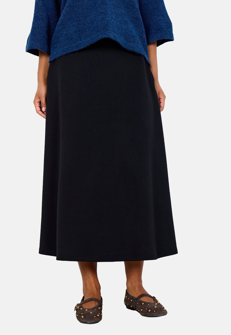 Black, knee-length, A-line skirt made of a soft material, paired with dark shoes featuring gold stud accents and a round toe.