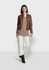 Brown leather bomber jacket with a zip closure, worn over a beige knit sweater, paired with cream wide-leg pants and black ankle boots.