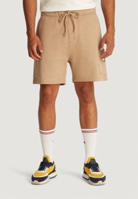 Pantaloni corti con coulisse beige, in tessuto misto cotone, con vita a costine. Abbinati a calzini bianchi con strisce rosse e blu e scarpe da ginnastica colorate.