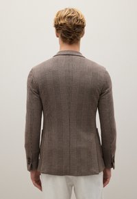 Brauner karierter Blazer mit strukturierter Passform, Schlitz hinten und taillierten Ärmeln. Aus einem strukturierten Stoff mit subtilen Musterdetails.
