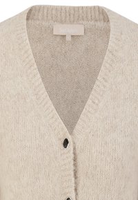 Cárdigan de punto en color beige con escote en V, textura suave y dos botones en la parte delantera. La etiqueta dice "Soft Rebels", talla S.
