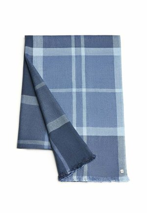 Blue plaid blanket featuring dark and light blue tones, woven texture, fringed edges, and a small logo detail in the bottom corner.