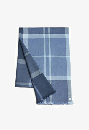 Blau kariertes Deckchen mit dunklen und hellen Blautönen, gewebter Textur, fransigen Rändern und einem kleinen Logodetail in der unteren Ecke.