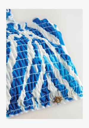 Modrý a bílý skládací materiál s vlnkovaným vzorem, který je na spodním lemu obohacený o dekorační bronzový prvek. Hladká textura s nařaseným detailem.