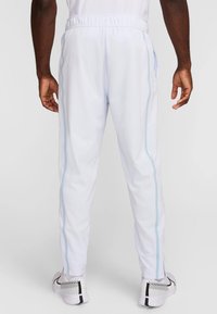 Bílé sportovní kalhoty se světle modrými pruhy po stranách, elastickým pasem a dvěma bočními kapsami, vyrobené z hladké syntetické tkaniny.