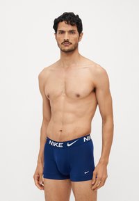 Mornarsko plave Nike bokserice od glatkog materijala, s bijelim brendiranim pojasom i prilagođenim dizajnom. Bez dodatnih uzoraka ili akcenata.