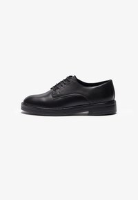 Black leather shoe with a rounded toe, featuring a smooth finish, six eyelets for laces, and a thick black rubber sole.