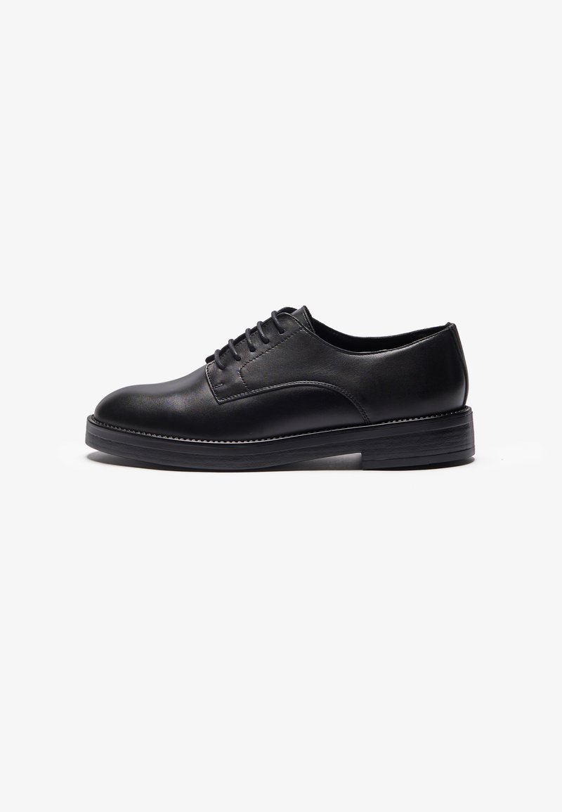 Black leather shoe with a rounded toe, featuring a smooth finish, six eyelets for laces, and a thick black rubber sole.