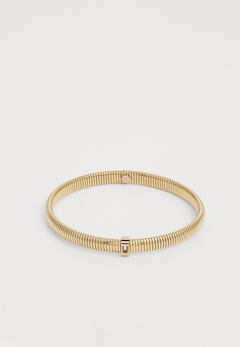 Bracelet flexible en ton doré avec fermoir intégré, présentant de petits détails rectangulaires rouges, blancs et noirs.