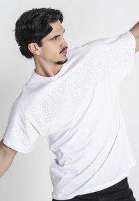 Weißes, übergroßes T-Shirt aus Baumwolle mit einem großen "GANNI KAVANAGH"-Textdesign in einem dezenten Muster an der Seite.