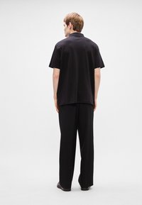 Camisa preta de manga curta com costas rectas e calças pretas largas. Textura de tecido suave, design minimalista. Sem padrões visíveis.