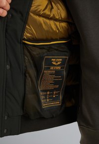 Giacca soft shell nera a due strati con una fodera isolante dorata e una tasca in rete. Include un'etichetta con le specifiche del prodotto.