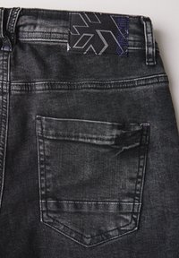 Jeans de mezclilla negros con un bolsillo trasero con un contorno triangular y una etiqueta con patrones geométricos en la cintura.