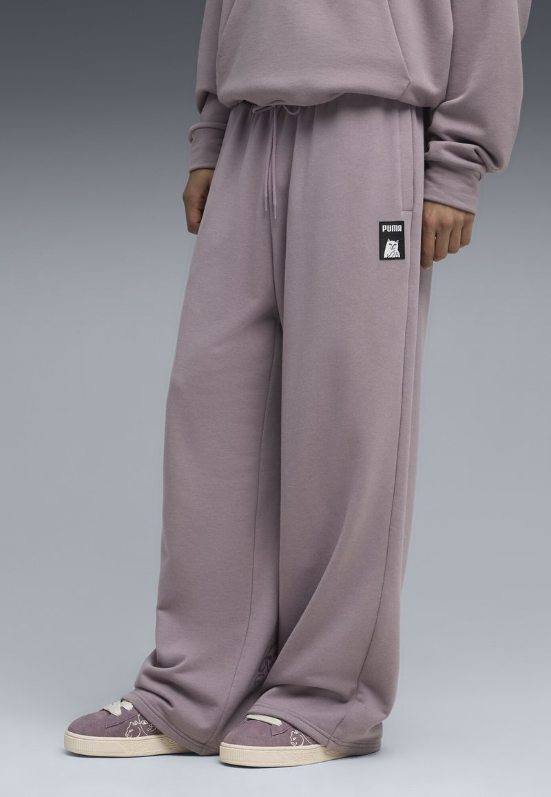 Pantalones deportivos de color púrpura claro con cintura elástica, bolsillos laterales y una etiqueta con el logo de Puma en negro. Corte suave y relajado con una textura lisa.