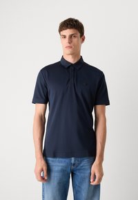 Camisola polo azul-marinho com mangas curtas, apresentando um colarinho e um logotipo discreto no peito. Feita de material suave e leve.