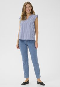 Blouse sans manches rayée bleue et blanche avec des épaules volantées, associée à un jean skinny bleu clair et des ballerines noires.