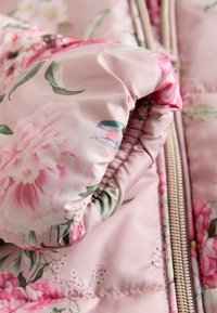 Blomstrede dunjakke med et lyserødt, blankt ydre stof. Har rynkede ærmer, en guldfarvet lynlås og et mønster af pink og grønne blomster.