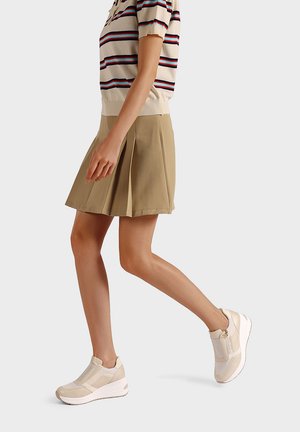 Gonna plissettata beige abbinata a una maglia a righe casual. Le calzature presentano un design testurizzato con chiusura lampo e suola a zeppa.