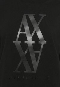 Must mustriga kangas, kus suured, läikivad "A|X|A|X" tähed on üksteisega kattuvad, ja allpool on väiksem "ARMANI EXCHANGE" tekst peene läikiva viimistlusega.
