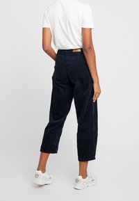 Marina kordflöjtsbyxor med avslappnad passform, kort längd och en bakpatchetikett. Bärs med en vit t-shirt och vita sneakers.