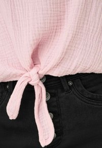 Lichtroze gekreukte katoenen top met een geknoopte voorkant, gecombineerd met zwarte denim met metalen knopen en een gladde textuur.