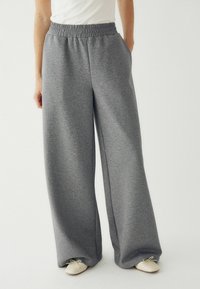 Szürke, bő szárú dizájnnal rendelkező sportnadrág, rugalmas derékkal, zsebekkel. Világos színű, hegyes orrú cipővel párosítva.