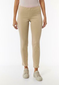 Beige stretchige Hosen mit einem figurschmeichelnden Design, schmal zulaufendem Bein und glatter Textur. Kombiniert mit hellen Sneakers. Minimale Details.