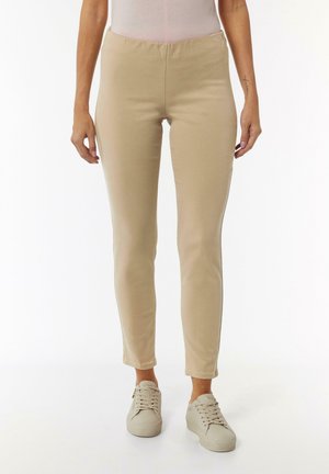 Beige stretchige Hosen mit einem figurschmeichelnden Design, schmal zulaufendem Bein und glatter Textur. Kombiniert mit hellen Sneakers. Minimale Details.