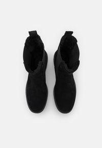 Bottes noires à la cheville avec un extérieur en textile doux, une doublure moelleuse et des panneaux latéraux élastiques pour un enfilage facile. Semelle plate avec un léger motif de traction.
