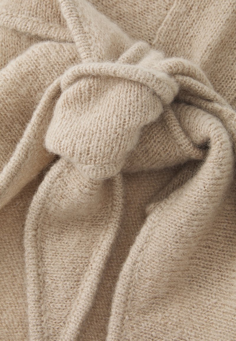 Beige strikket stof med en blød, plysset tekstur, der har et knyttet design og synlige syningsdetaljer.