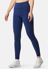 Marina blå leggings gjorda av stretchigt tyg, med hög midja och en slät textur. Kombinerat med vita träningsskor.