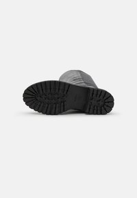 Suela de bota de goma negra con surcos profundos, que presenta una superficie texturizada y un diseño de punta redonda, adecuada para ofrecer tracción en diversas superficies.