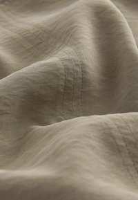 Primo piano di un tessuto beige con morbide pieghe e linee di cucitura parallele visibili.