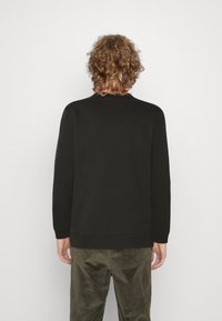 Sudadera negra con cuello redondo y mangas largas, hecha de un material liso. La parte trasera presenta un diseño simple sin adornos visibles.