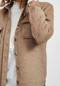 Bruine wollen blend overhemdjacket met een knoopsluiting aan de voorkant, twee borstzakken en een ronde kraag, met een zachte structuur en contrasterende knopen.