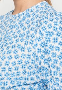 Tissu à imprimé floral bleu avec de petites fleurs sur fond blanc, présentant une texture douce et une coupe décontractée près de l'encolure.