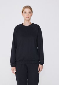 Sudadera negra de mangas largas, con cuello redondo y cintura elástica. Confeccionada en una tela suave con una textura lisa y diseño de mangas raglán.