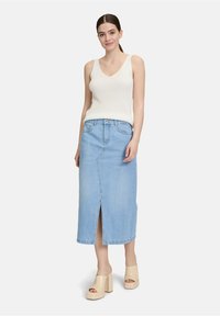 Lichtblauwe denim maxi rok met een voorzijdige split, gecombineerd met een aansluitend wit geribbeld tanktop en beige plateauhakken.